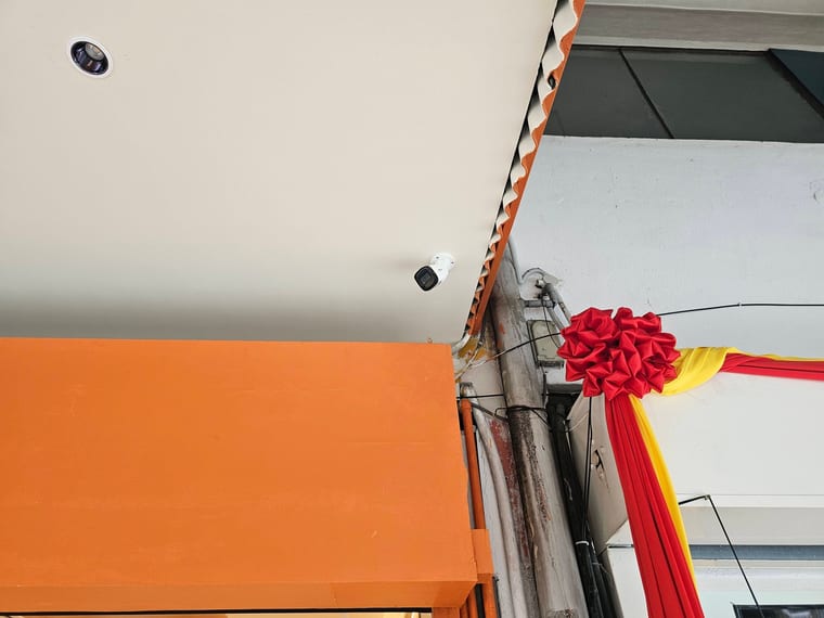 A small camera on a white ceiling above an orange shopfront.