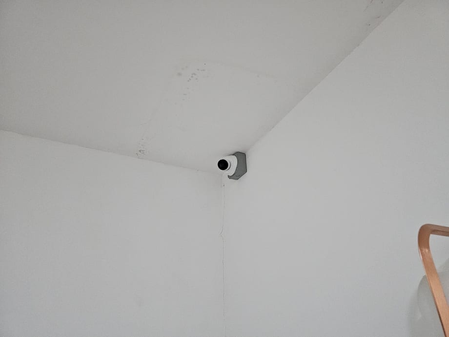 A bullet camera mounted in the corner of a white ceiling.